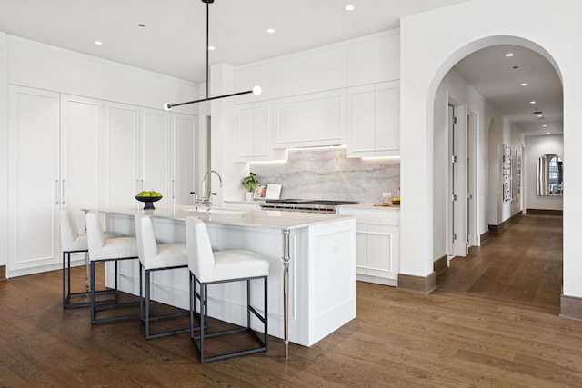 kitchen with decorative backsplash, dark wood-type flooring, white cabinets, a kitchen island with sink, and a sink