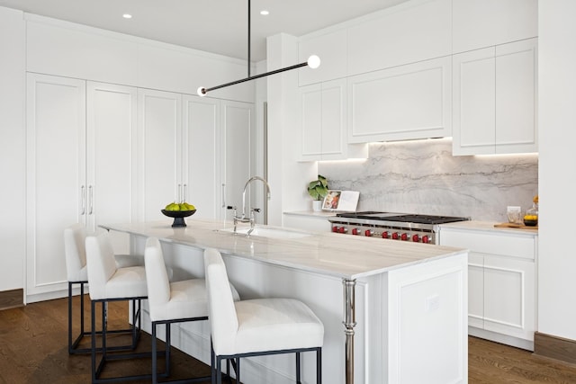 kitchen featuring light stone counters, a sink, white cabinetry, range, and an island with sink