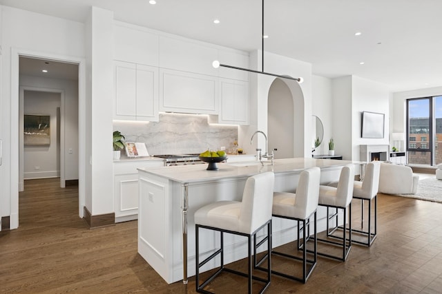 kitchen featuring white cabinets, an island with sink, open floor plan, a kitchen bar, and backsplash