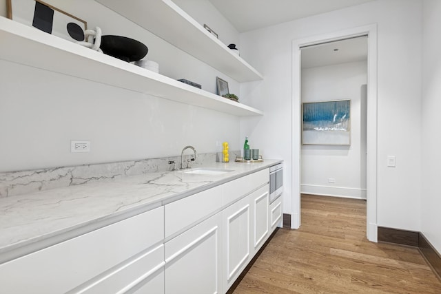 interior space featuring a sink, white cabinetry, light stone countertops, open shelves, and stainless steel microwave