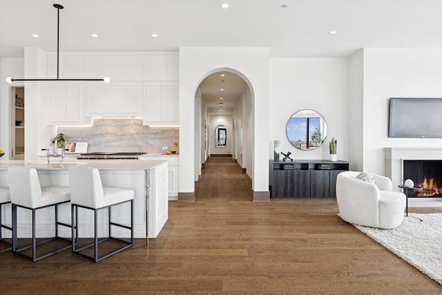 kitchen with arched walkways, a center island with sink, open floor plan, white cabinetry, and a lit fireplace