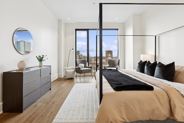 bedroom with baseboards, a city view, recessed lighting, and light wood-style floors