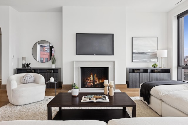 living area with arched walkways, a lit fireplace, and wood finished floors