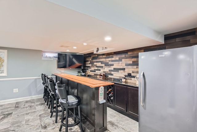 bar with butcher block counters, wood walls, and fridge