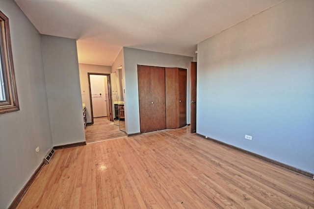 unfurnished bedroom with ensuite bath, a closet, and light wood-type flooring