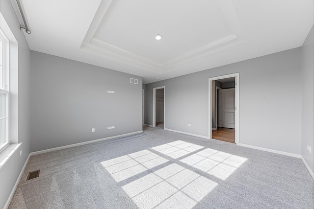 unfurnished bedroom featuring a closet, a walk in closet, light colored carpet, and a tray ceiling