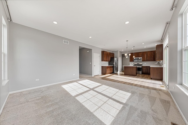 kitchen featuring a kitchen island, appliances with stainless steel finishes, sink, hanging light fixtures, and light carpet