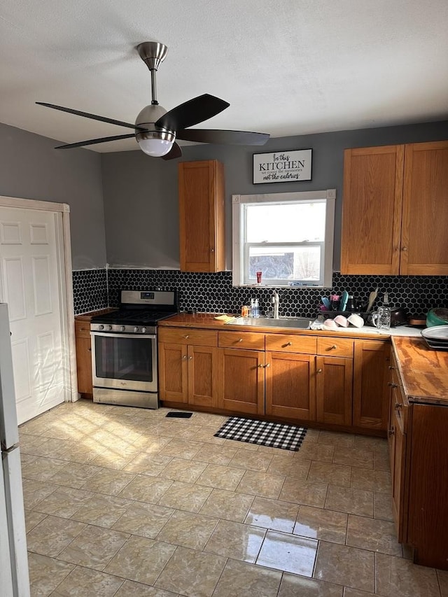 kitchen featuring white fridge, sink, stainless steel gas range oven, ceiling fan, and butcher block countertops