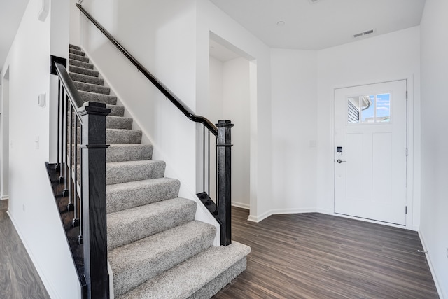 entrance foyer with stairs, dark wood-type flooring, visible vents, and baseboards