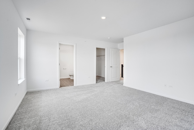 unfurnished bedroom with baseboards, visible vents, connected bathroom, a walk in closet, and carpet flooring