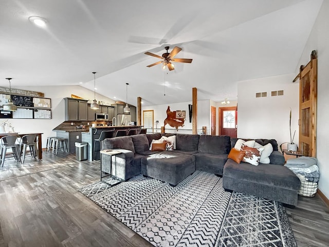 living room with ceiling fan, a barn door, dark hardwood / wood-style flooring, and vaulted ceiling