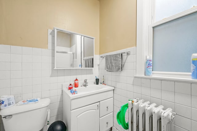 bathroom with toilet, tile walls, vanity, and radiator heating unit