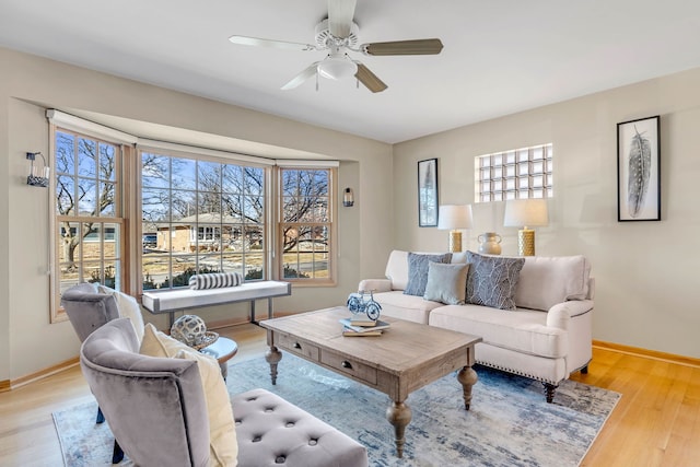 living area with a ceiling fan, light wood-style flooring, and baseboards