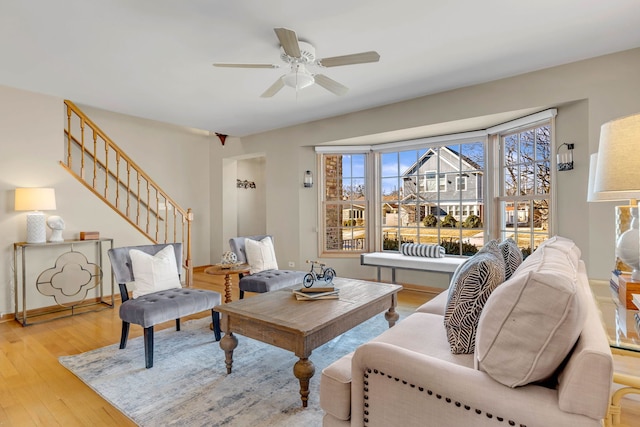 living area with light wood-type flooring, stairs, baseboards, and a ceiling fan