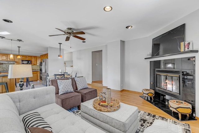 living area with recessed lighting, a fireplace, a ceiling fan, baseboards, and light wood finished floors