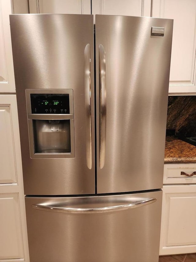 interior details with backsplash, dark stone counters, white cabinets, and stainless steel refrigerator with ice dispenser