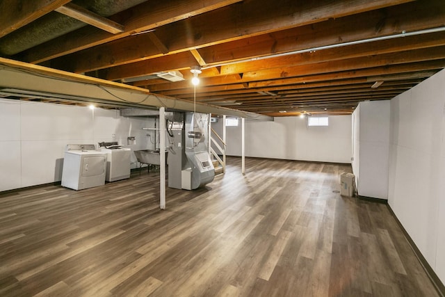 basement featuring heating unit, sink, dark wood-type flooring, and washer and clothes dryer