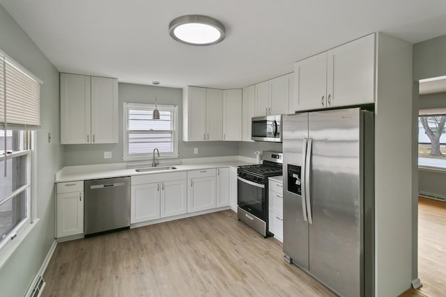 kitchen featuring appliances with stainless steel finishes, sink, white cabinets, hanging light fixtures, and light wood-type flooring