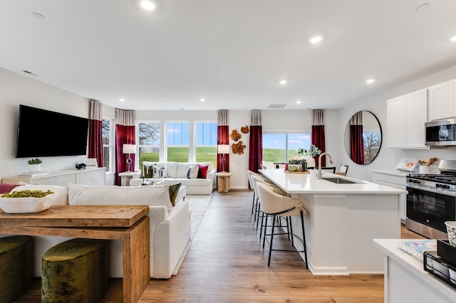 kitchen featuring white cabinets, stainless steel appliances, an island with sink, sink, and light wood-type flooring