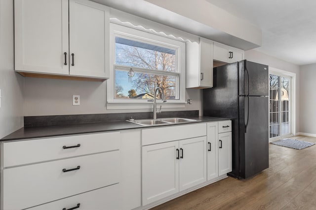 kitchen featuring white cabinetry, sink, black refrigerator, and light wood-type flooring