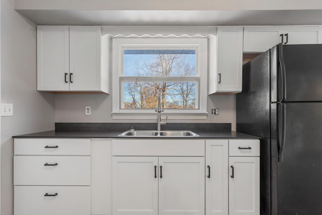 kitchen featuring black refrigerator, sink, and white cabinetry