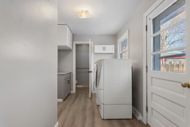 washroom featuring cabinets, washing machine and clothes dryer, and light hardwood / wood-style flooring