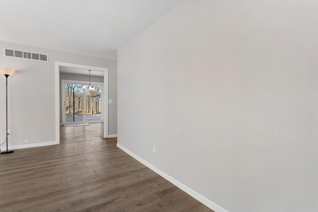 empty room with dark hardwood / wood-style flooring and a notable chandelier