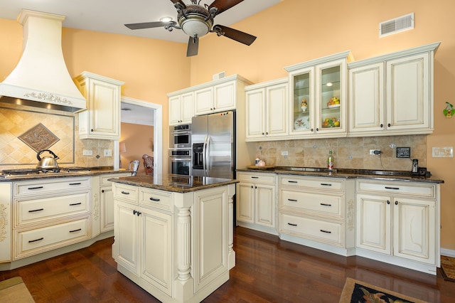 kitchen featuring a center island, stainless steel appliances, dark stone countertops, decorative backsplash, and custom range hood