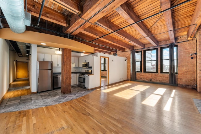 unfurnished living room featuring beam ceiling, light wood-type flooring, wooden ceiling, and brick wall