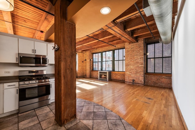 kitchen with beamed ceiling, brick wall, appliances with stainless steel finishes, and white cabinets