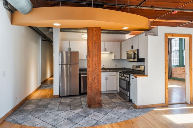 kitchen featuring stainless steel appliances, sink, white cabinetry, wood-type flooring, and brick wall