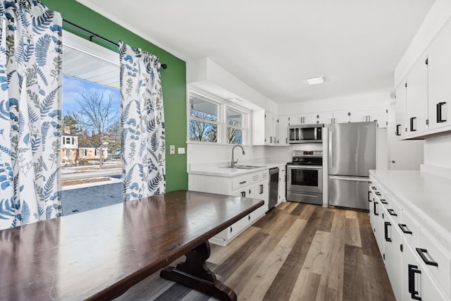 kitchen with a sink, light countertops, appliances with stainless steel finishes, white cabinetry, and dark wood-style flooring