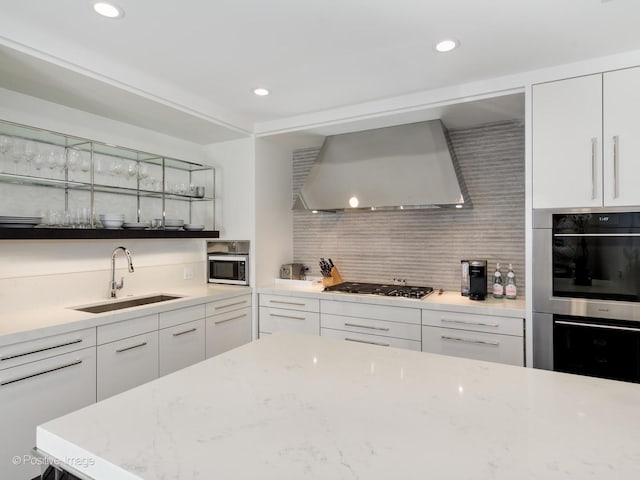 kitchen with white cabinets, appliances with stainless steel finishes, wall chimney range hood, sink, and backsplash