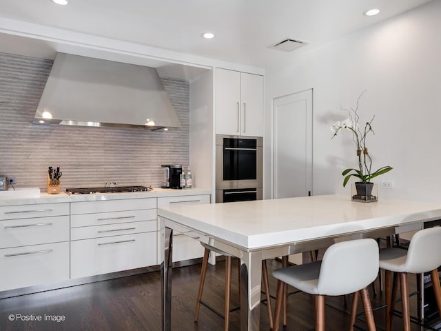 kitchen with white cabinetry, stainless steel appliances, dark hardwood / wood-style floors, backsplash, and wall chimney exhaust hood