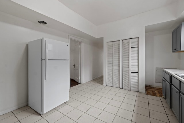 kitchen with light tile patterned flooring, white refrigerator, and gray cabinetry