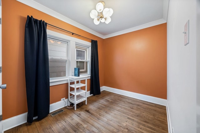 empty room featuring an inviting chandelier, ornamental molding, and hardwood / wood-style floors