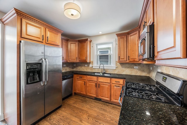 kitchen with sink, tasteful backsplash, appliances with stainless steel finishes, hardwood / wood-style flooring, and dark stone counters