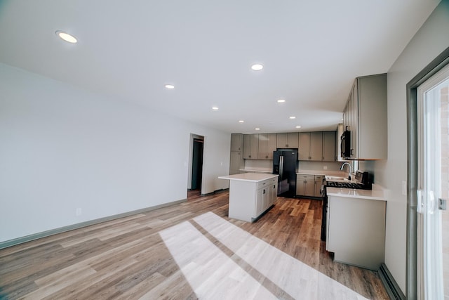 kitchen with gray cabinets, black fridge, a center island, light wood-type flooring, and range with gas stovetop