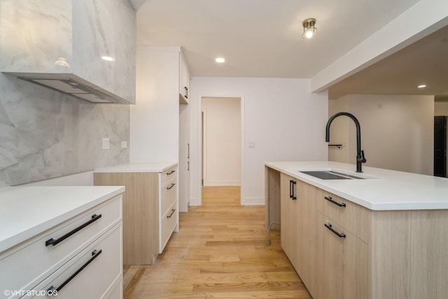 kitchen featuring sink, backsplash, light wood-type flooring, and an island with sink