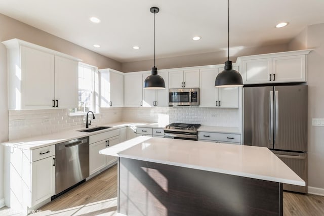 kitchen featuring hanging light fixtures, appliances with stainless steel finishes, sink, white cabinetry, and a kitchen island