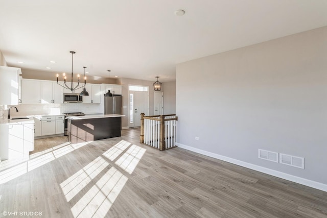 kitchen featuring appliances with stainless steel finishes, decorative light fixtures, white cabinetry, a center island, and decorative backsplash