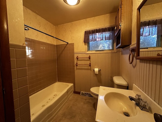 full bathroom with tile patterned flooring, sink, tiled shower / bath combo, toilet, and wood walls