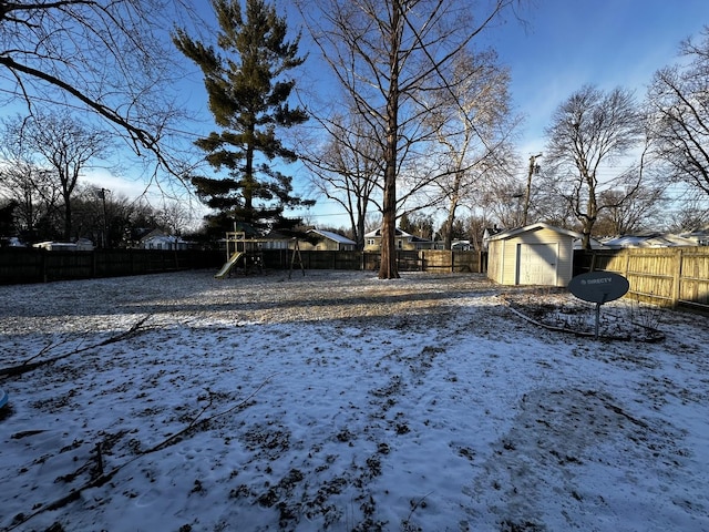 snowy yard featuring a playground and a storage shed