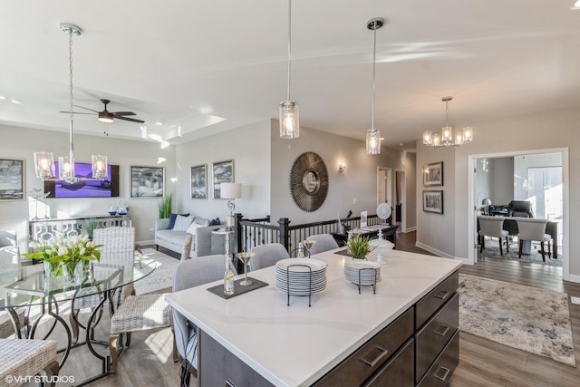 kitchen featuring decorative light fixtures, dark wood-type flooring, ceiling fan with notable chandelier, a kitchen island, and dark brown cabinetry