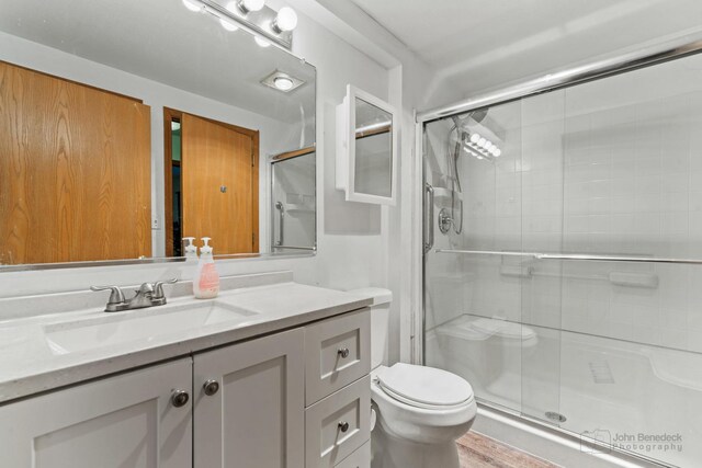 bathroom featuring hardwood / wood-style flooring, toilet, a shower with door, and vanity