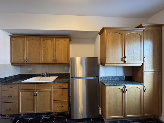 kitchen with stainless steel fridge, dark tile patterned floors, sink, dark stone countertops, and decorative backsplash