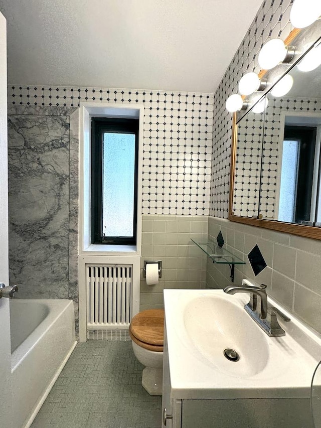 bathroom with radiator heating unit, vanity, tile walls, a tub to relax in, and toilet