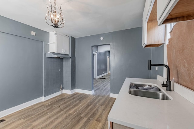 kitchen with decorative light fixtures, white cabinetry, sink, light hardwood / wood-style floors, and an inviting chandelier