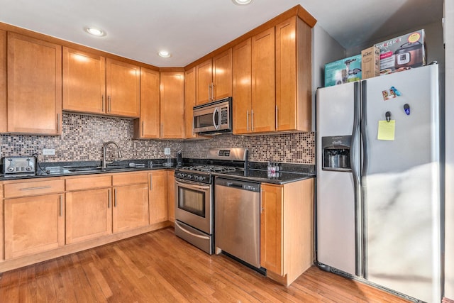 kitchen featuring sink, light hardwood / wood-style flooring, dark stone countertops, and appliances with stainless steel finishes