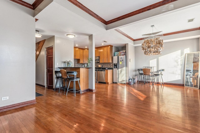 kitchen featuring crown molding, appliances with stainless steel finishes, tasteful backsplash, hardwood / wood-style floors, and a notable chandelier